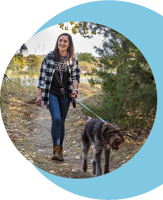 A woman walking her dog through a trail.