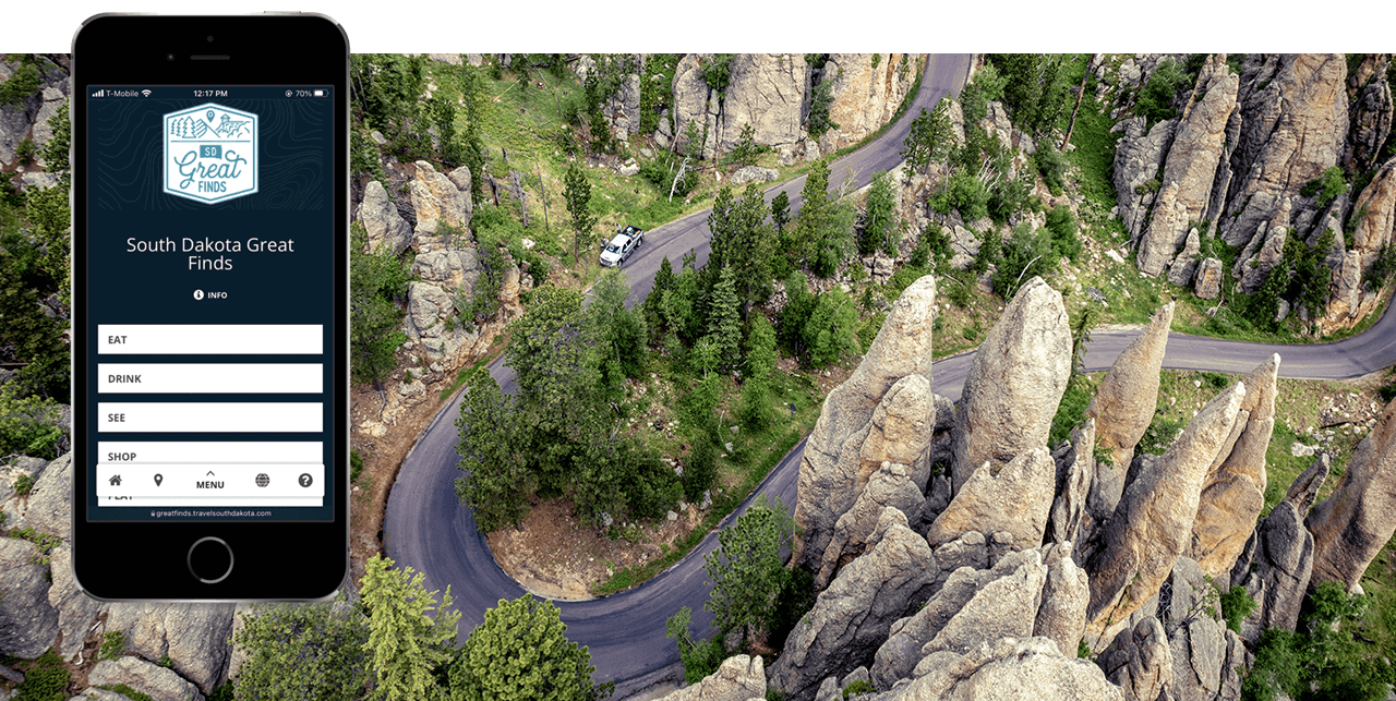 A Phone with the Great Finds app displayed; on a backdrop image of an arial view of a road winding through the forest.