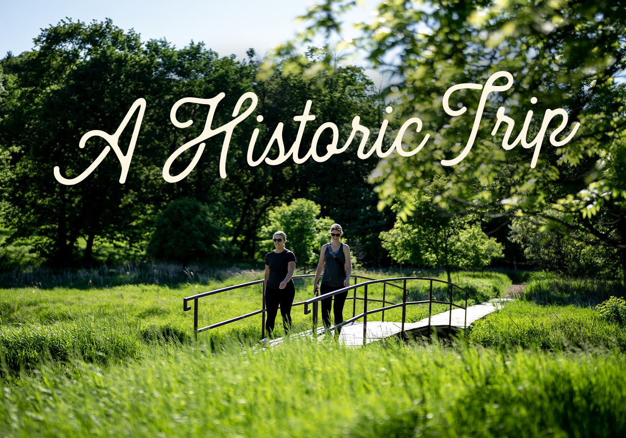 Two women walk along a boardwalk bridge. A headline reads: A historic trip.