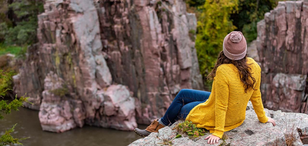 A woman sitting on the edge of a cliff over a lake.