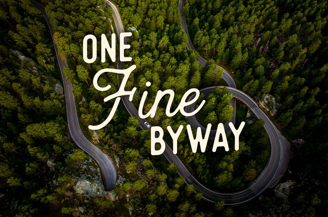 A winding road through a lush forest. A headline reads: One Fine Byway