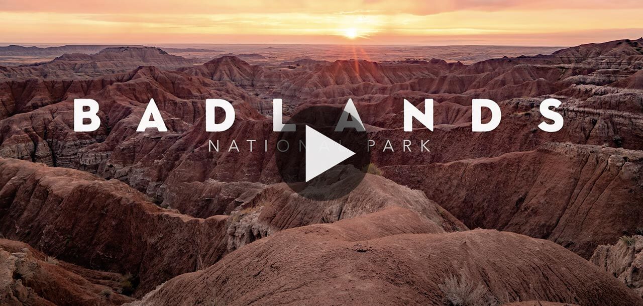 The opening still of the video 'Badlands National Park' featuring a sun rising on the horizon with a landscape of rocky terrain.
