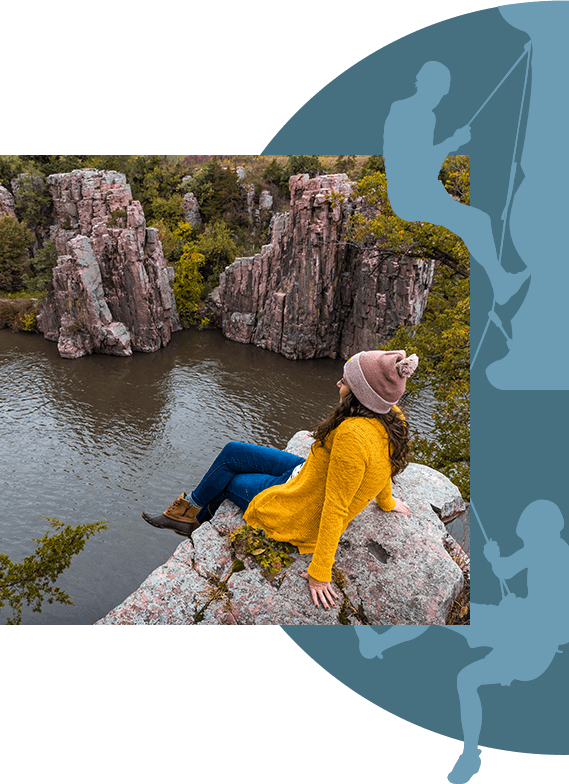 A woman sitting atop a rock formation on the bank of a river.