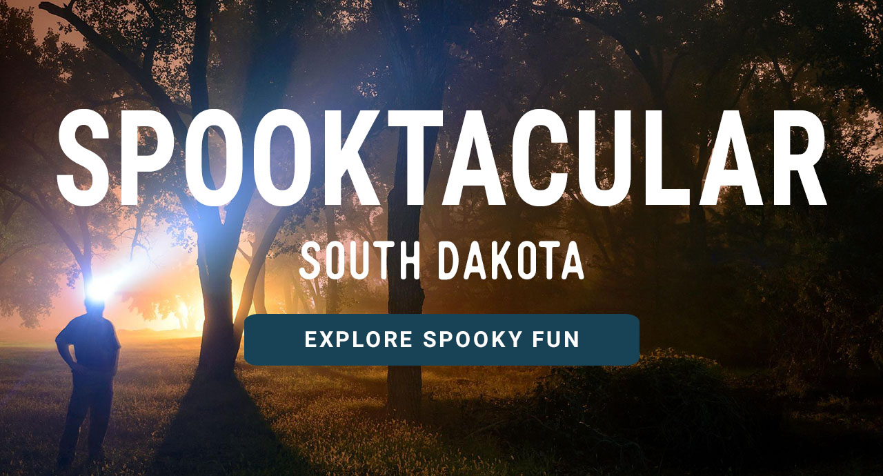 A man exploring a forest at night. A headline reads: Spooktacular South Dakota. Explore Spooky Fun.