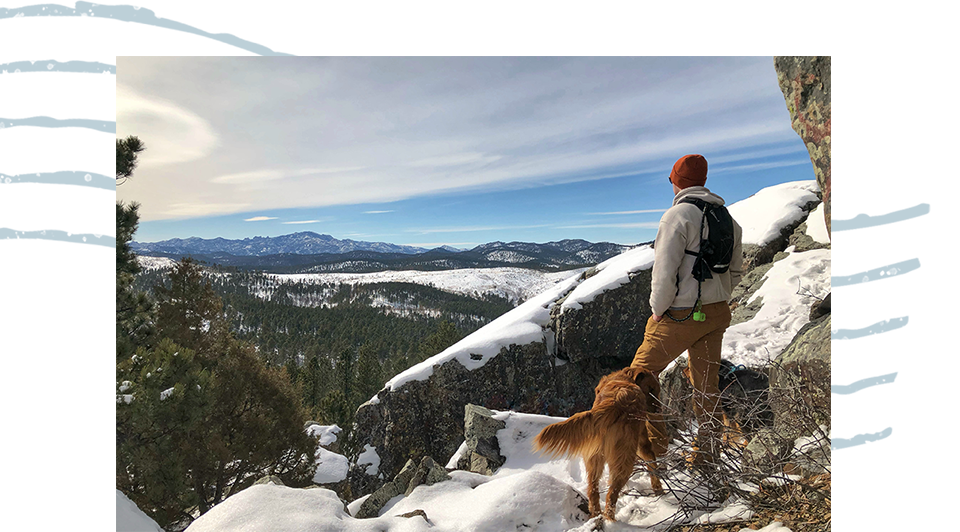 A man and his dog sitting on top of a mountain overlooking the valley below.
