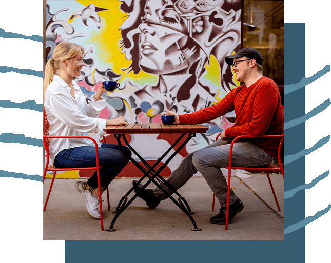A couple sitting at an outside table drinking coffee.