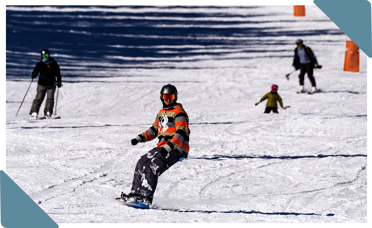 Snowboarders and skiers skiing down a slope of packed snow.